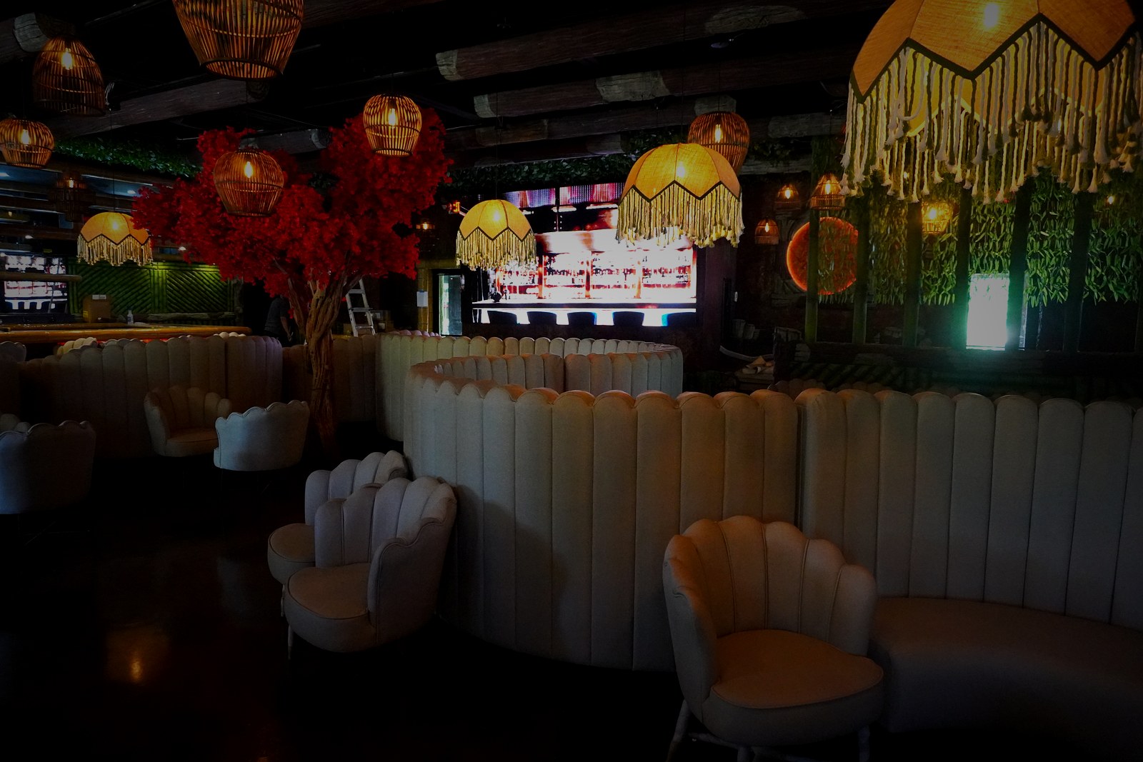 Casa Tequila Prime main lounge — scalloped seating, red flowering trees, and amber pendants